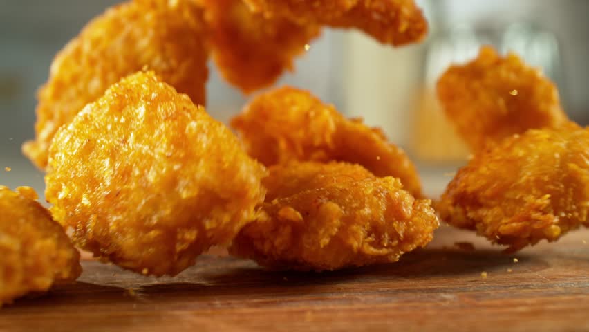 4K slow motion video of crispy chicken nuggets dropping onto a flat surface. Perfect for fast food, snack, commercial, or food styling content.