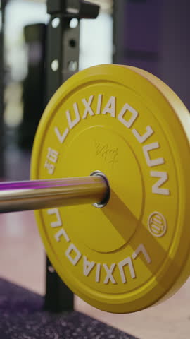 Close-up of yellow weight plate being added to barbell. Gym, fitness, workout, strength training, body building, exercise, weights, health, wellness, lifestyle. fitness, workout, gym and sport