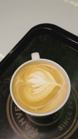 Barista crafts delicate latte art in a warm coffee shop setting – watch the transformation of a simple drink into a work of art