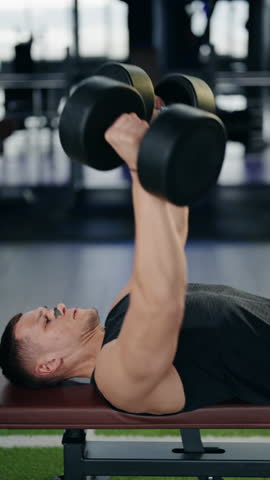 A muscular man performs dumbbell bench presses in a modern gym. He focuses on his form and breathing, demonstrating strength and dedication to fitness. healthy lifestyle and workout routine.
