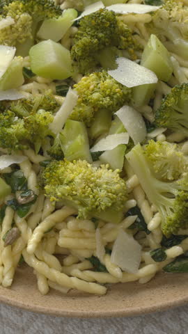 Trofie pasta with roughly chopped pesto, broccoli, and parmesan, background texture. Vertical video.
