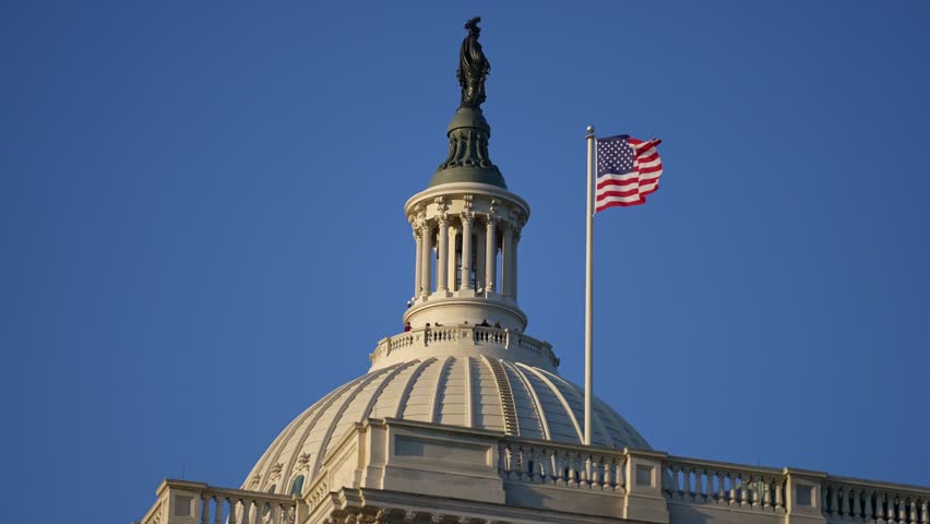 American flag waving near Congress Capitol dome in Washington DC. USA symbol. United States flag on Capitol. Flag against sky in Capitol. Flying American flag. Vote for freedom. Capitol Hill flags.