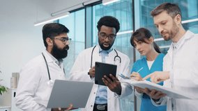 Multiracial team of doctors and nurses, standing close and discussing diagnosis, reviewing notes and tablet, wearing white lab coats and scrubs, in modern office. Diverse healthcare professionals. - Powered by Shutterstock - Get 15% off with code: PIKWIZARD15