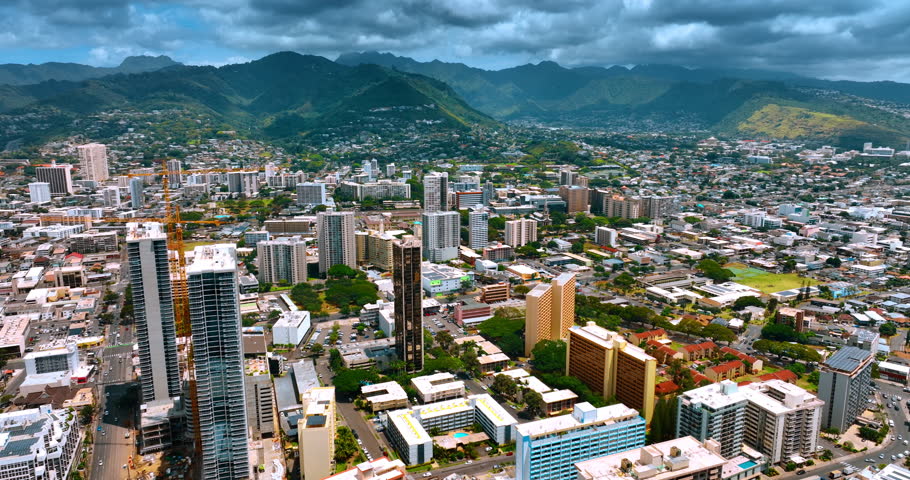 Panorama of modern beautiful Honolulu, Hawaii. Verdant mountains surrounding the city are covered with dark cloudscape. Aerial view.