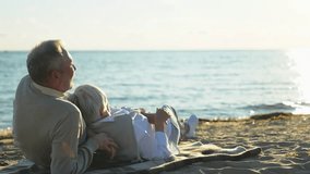 Senior mature couple sitting on beach hugging enjoying outdoor recreation. Old husband wife embracing with tenderness love enjoying sweet bonding. Grandmother grandfather together. Family moment love - Powered by Shutterstock - Get 15% off with code: PIKWIZARD15