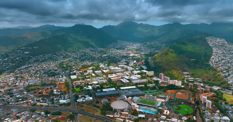 Rainy clouds gathered above Honolulu surrounded by verdant mountains. Drone footage approaching the stadium of University of Hawaii. Honolulu aerial view.