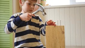 Kid hammers nails to wood with a hammer. Little boy helping with toy tools. Funny 6 years child having fun on building. Kid hammering crafting stuff using wooden pieces. Carpentry and family concept - Powered by Shutterstock - Get 15% off with code: PIKWIZARD15