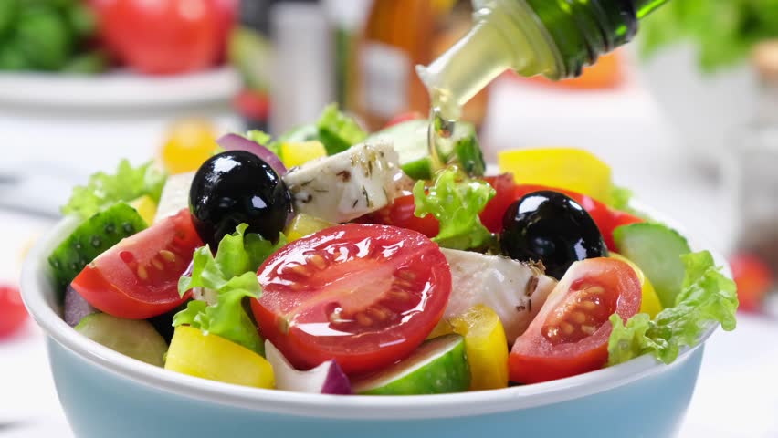Salad being drizzled with olive oil from a bottle, bowl of fresh Greek salad close-up