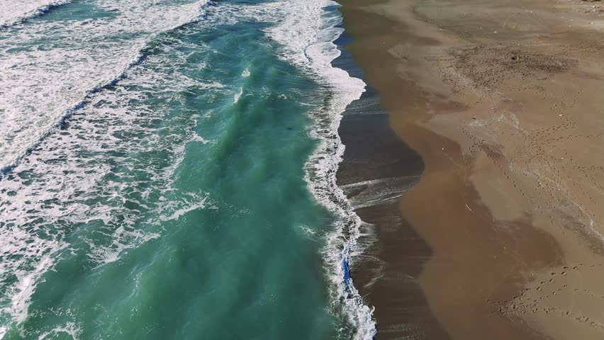 Turquoise ocean waves rolling, gently crashing onto sandy shoreline, revealing rhythmic marine energy and serene coastal landscape