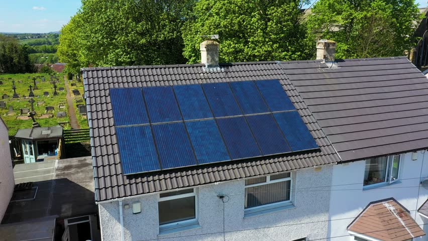 Aerial drone footage of a British semi detached house with energy saving solar panels on the roof on a sunny summers day located with a grave yard behind the house
