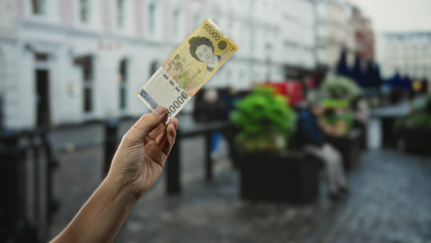 Man holding south korean won banknote on a busy city street, showcasing financial elements in an urban outdoor setting.