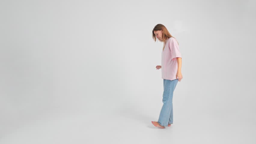 Woman is walking stepping on bare heels holding hands on sides trying to keep balance. Young adult Caucasian lady is doing physical exercise for healthy feet filmed in slow motion on white background.