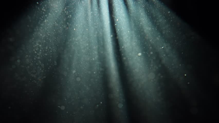Deep underwater scene with floating particles in blue haze, creating a calm and mysterious atmosphere. Slow motion. A beam of light falling into the water highlights the floating particles. Slow