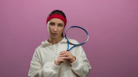 Woman holding tennis racket in white attire against pink background looking thoughtful with headband displaying contemplation over isolated setting involving sports equipment. - Powered by Shutterstock - Get 15% off with code: PIKWIZARD15