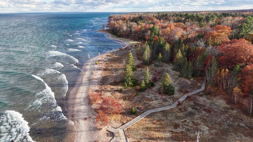 Dramatic aerial view of a forested Great Lakes bluff with crashing waves and vibrant fall foliage