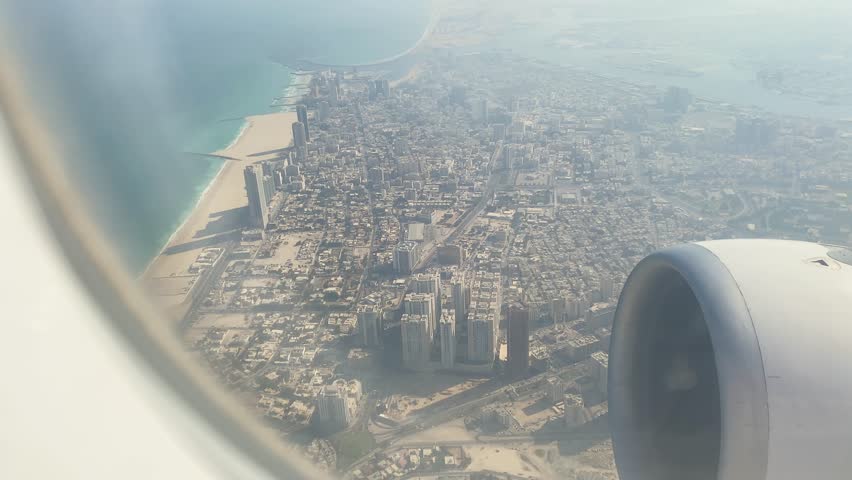 Passengers window Aerial point of view Abu Dhabi’s sunlit sandy beach coastline from plane window during stopover flight. Clear skies, turquoise waters, modern cityscape of UAE from above