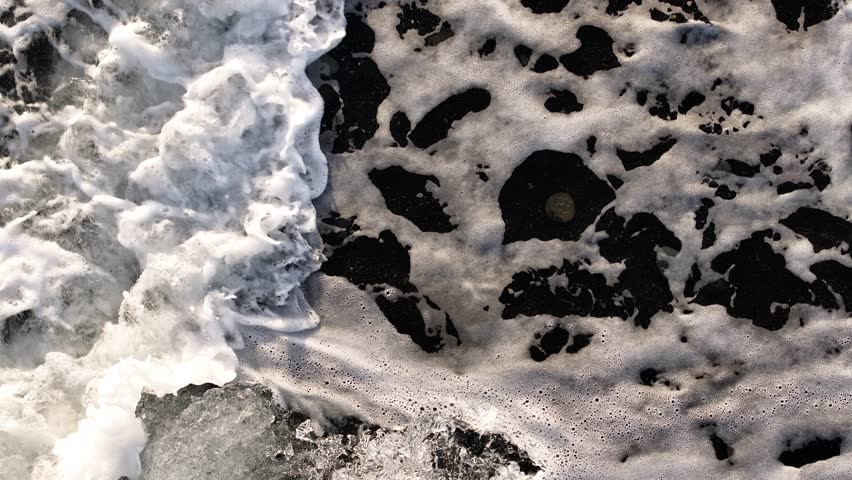 Waves crash over the black pebbled shore of Diamond Beach in Jökulsárlón, Iceland.