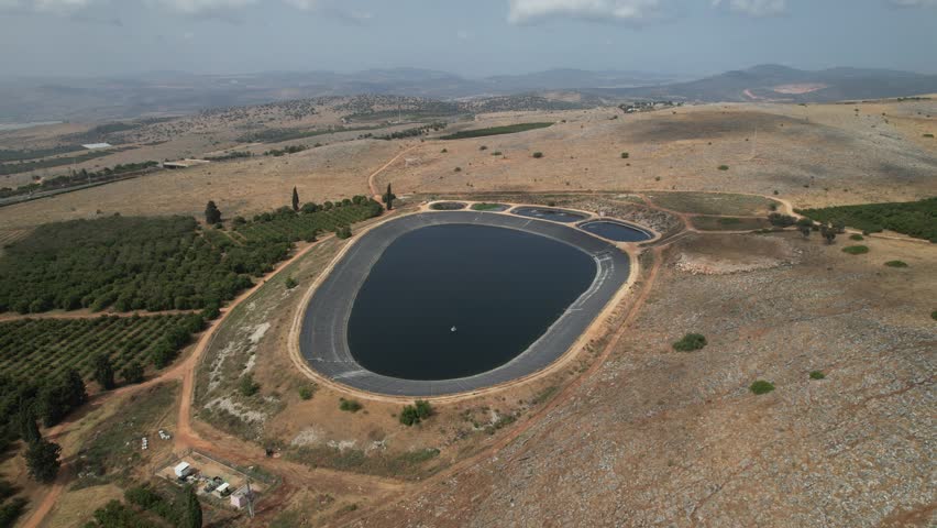 Aerial shot of a large artificial water reservoir surrounded by arid terrain and patches of greenery, emphasizing water management in dry regions. Israel