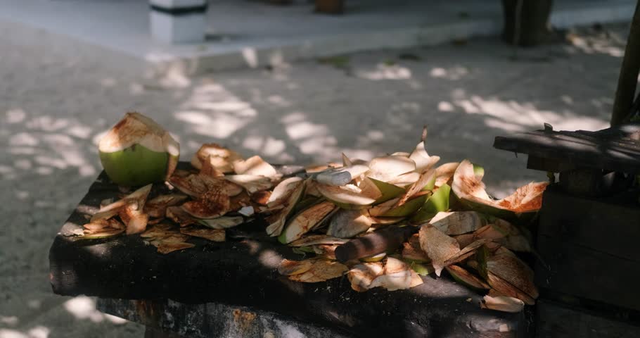 View of a table where coconut husks are cut to prepare coals for a grill. On the table is a green coconut shell and a machete. Tropical life on the beach.
