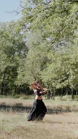 A talented tribal dancer demonstrates her expertise in an open field surrounded by lush greenery. Clad in a flowing outfit, she gracefully moves to the rhythm of nature in daylight.