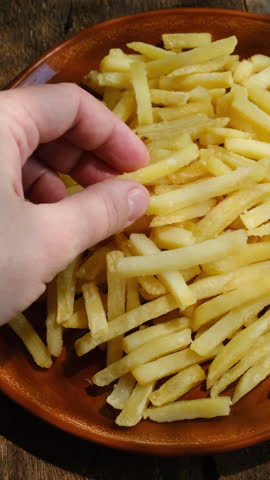 Vertical video. Woman is enjoying french fries. Fast food, greasy snack.