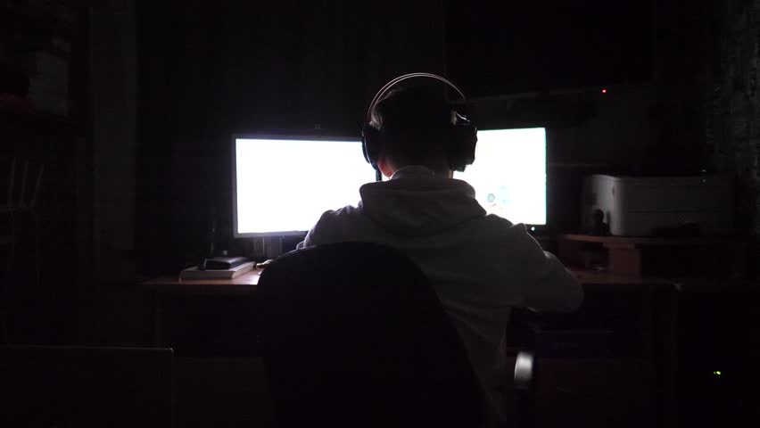 Male gamer playing in first person shooter on computer at home. Young man in headphones spending time at online video game on pc at night. Concept of cyberspace, competition and tournament. Slow mo