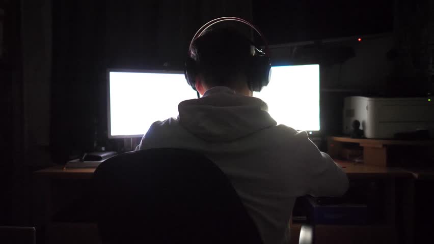 Male gamer playing in first person shooter on computer at home. Young man in headphones spending time at online video game on pc at night. Concept of cyberspace, competition and tournament. Slow mo