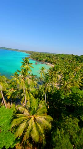 Cinematic FPV drone flight over tropical beach with palm trees, white sand, and crystal-clear turquoise sea on Koh Kood island in Thailand. Aerial view of exotic coastline and paradise landscape.