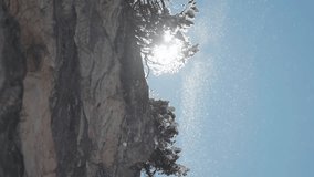 Sunlight pierces through the branches of snow-covered trees hanging on the rocky cliff, as snow particles drift in the crisp sky. Slow-motion parallax video. - Powered by Shutterstock - Get 15% off with code: PIKWIZARD15