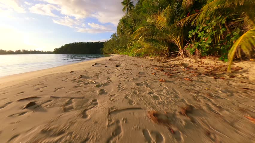 FPV drone flying low over tropical beach with golden sand, palm trees, and ocean waves at sunset on remote island in Thailand. Ideal for travel, freedom, and summer nature themes.