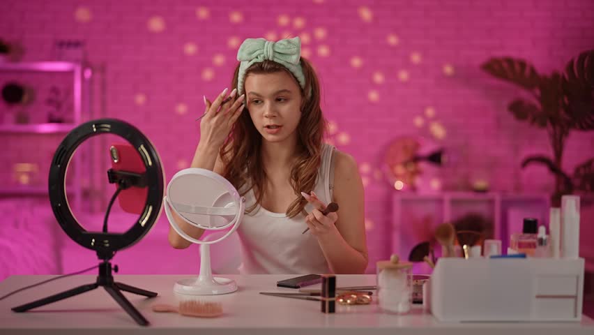A cheerful individual is sitting at a makeup desk surrounded by beauty products, ready for a captivating video session.