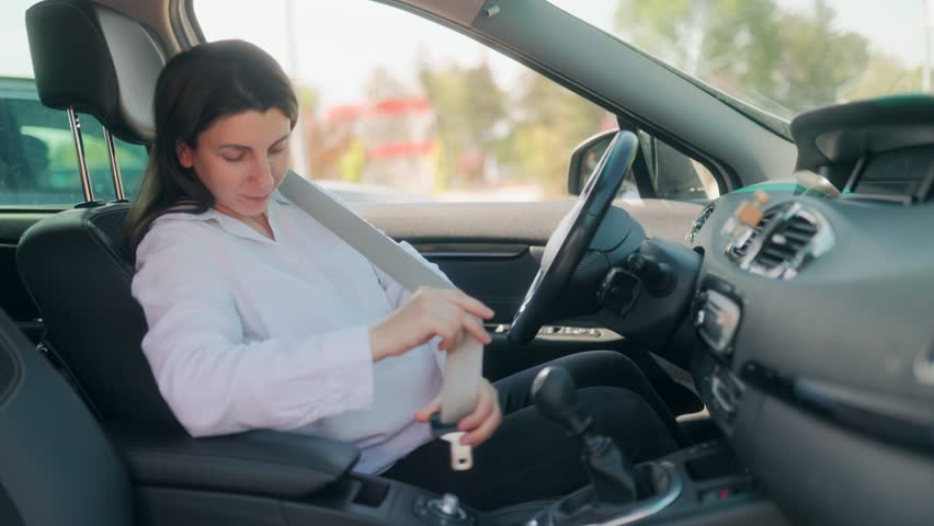 Expecting mother buckling up her seatbelt inside a parked car, placing safety first for both herself and her unborn child in a calm, everyday driving scenario.