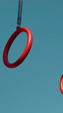 Strong athletic man jumping and waving on gymnastic rings, close up of rings. Male doing exercises on ring on sports ground outdoors. Vertical video