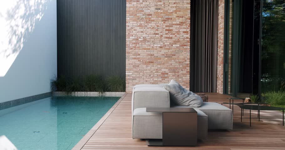 Stylish outdoor relaxation area featuring a comfortable lounge chair, elegant furniture, and a serene pool by a brick wall home with large sliding doors and lush greenery. Modern Home Exterior