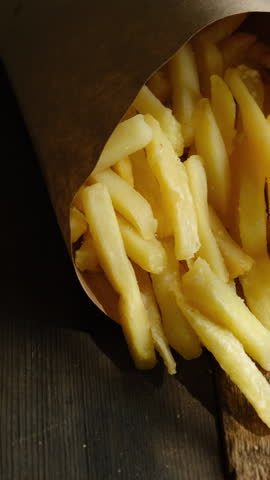 Vertical video. Street food. French fries fast food in paper box on wooden background.
