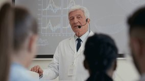Medium shot from audience space of senior male clinical professor equipped with earset microphone delivering lecture in auditorium sharing latest developments with colleagues during group seminar - Powered by Shutterstock - Get 15% off with code: PIKWIZARD15