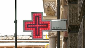 A red pharmacy neon cross pulses rhythmically against the sky, viewed from a low angle in a quiet Rome street - Powered by Shutterstock - Get 15% off with code: PIKWIZARD15