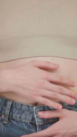 VERTICAL VIDEO: Close-up of a young woman gently touching her stomach, symbolizing gut health, probiotics, digestive wellness, healthy lifestyle and Eating. Concept of women's health and prevention.