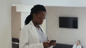 Static shot of Black female healthcare worker text messaging on mobile phone then answering incoming call while standing in clinic hallway then walking off camera - Powered by Shutterstock - Get 15% off with code: PIKWIZARD15