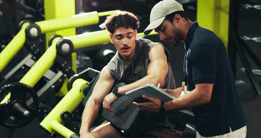 Men, personal trainer and tablet with machine for workout routine, training or exercise schedule at gym. Male people, fitness instructor or coach with technology or checklist for health goals or app