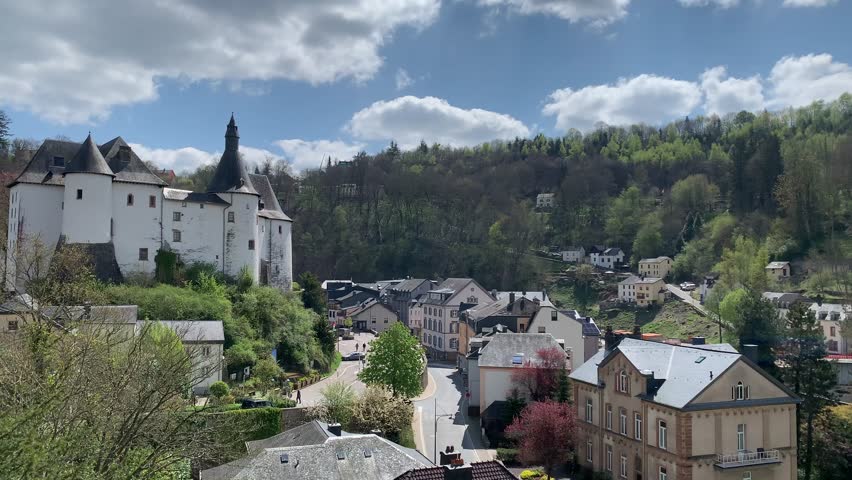 Panoramic, scenic view of Clervaux Castle (Chateau) and Clervaux town houses. People are walking at city centre. Motion of car. Clervaux, Luxembourg