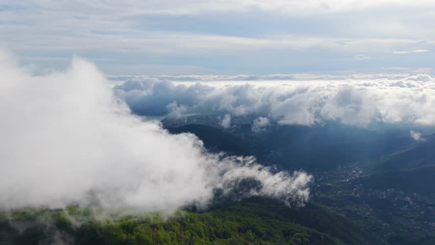 Big clouds floating above green mountain slopes with an aerial view of the landscape