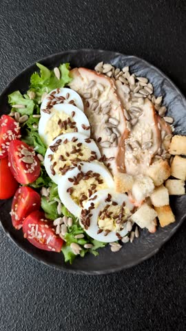 Bowl with caesar salad with chicken, parmesan cheese, tomatoes, croutons, lettuce leaves, flax seeds, sunflower and sesame seeds