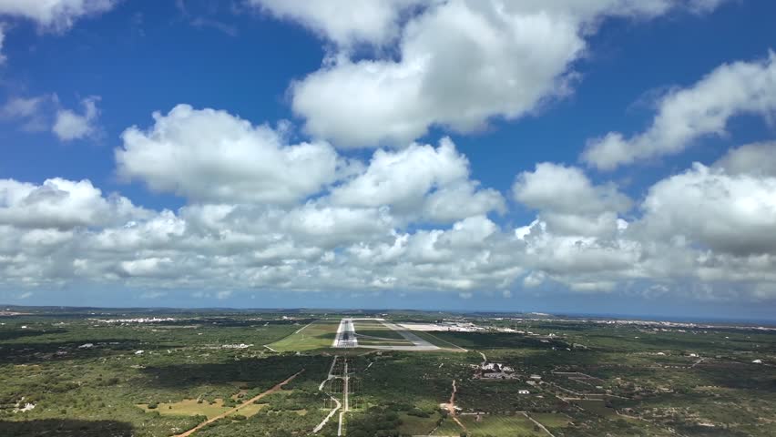 A pilot perspective POV FPV to Menorca Airport runway 01, under a blue sky with cottony clouds and the shadows on the runway.