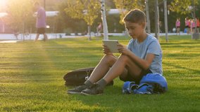 schoolboy relaxes on the grass enjoying digital leisure on a tablet. Digital leisure combines gadget time and technological leisure after active play outdoors, balancing screen use physical activity. - Powered by Shutterstock - Get 15% off with code: PIKWIZARD15