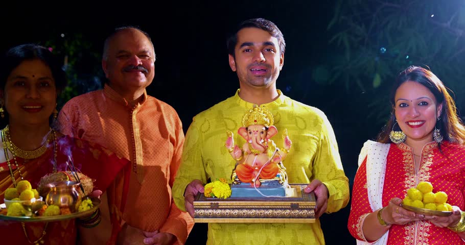 Welcoming clay idol of Lord Ganesha during Ganesh Chaturthi by Indian family with senior parents and young couple bringing Ganpati home for worship with laddu, puja thali at decorated house entrance