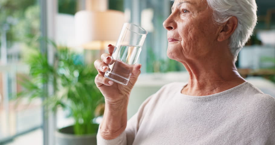Drinking, water and senior woman in home for wellness, health and nutrition in living room. Retirement, morning and elderly person with liquid, fluid and minerals for thirsty, hydration and detox