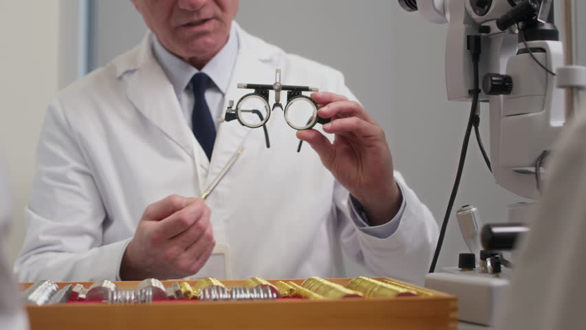 Close up on hands of mature male ophthalmologist holding trial frames consulting patient on prescription glasses while changing dioptric lenses during appointment at eye care clinic