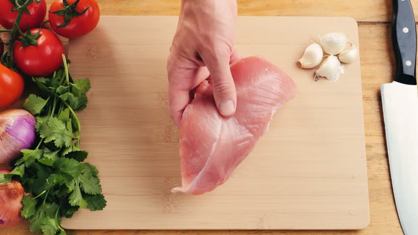 Man slicing raw turkey or chicken meat fillet on oak cutting board closeup, cooking with knife on restaurant kitchen.
