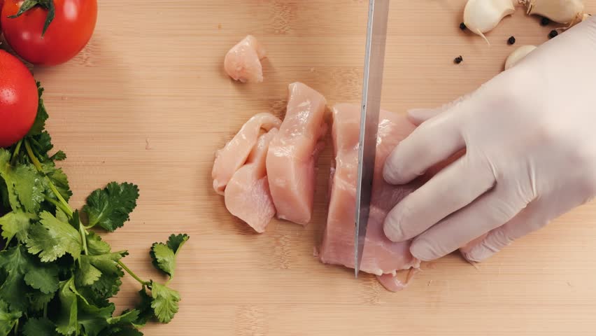 Man slicing raw turkey or chicken meat fillet on oak cutting board closeup, cooking with knife on restaurant kitchen.